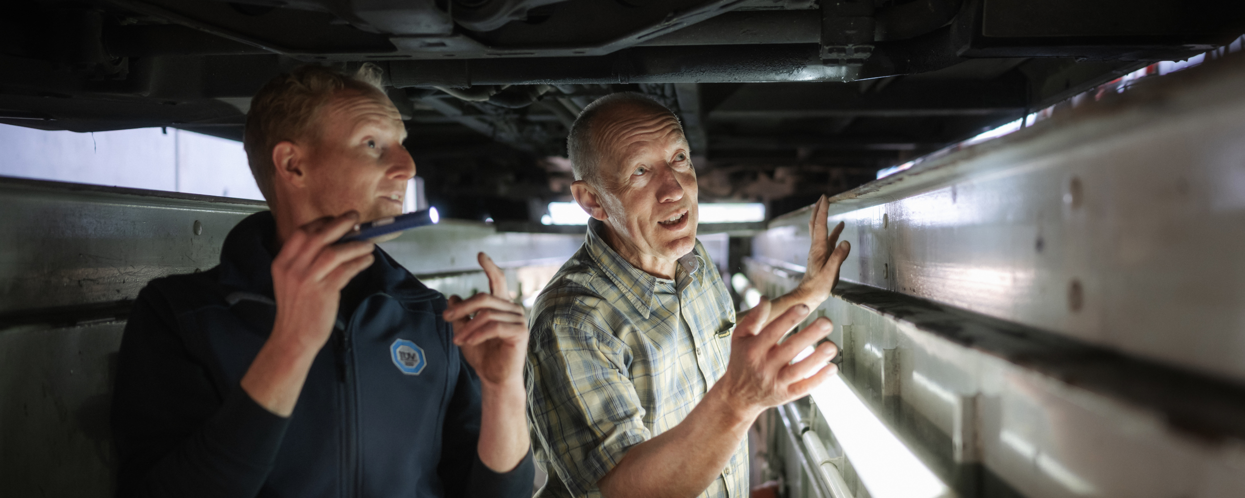 Zwei Werkstattmitarbeiter inspizieren einen Bus von der Unterseite