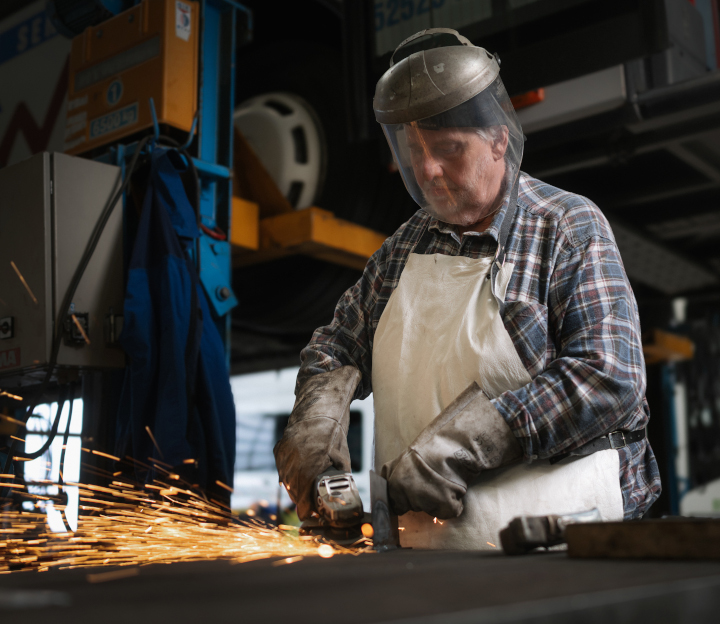 Handwerk Ein Werkstattmitarbeiter schleift oder sägt ein Metallteil. Es fliegen Funken